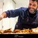A chef drizzles oil on food while wearing an apron and gloves in a kitchen in Amsterdam, The Netherlands